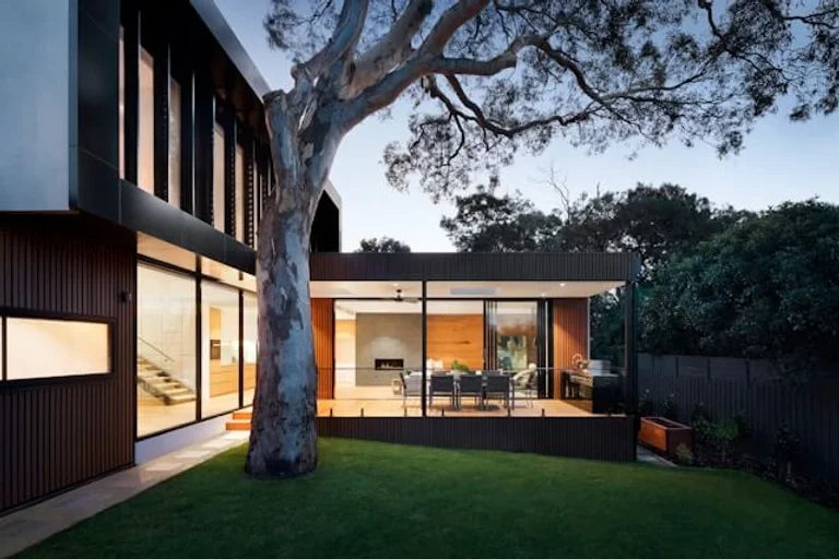 A contemporary Australian home at sunset with a gumtree in the yard and illuminated interior with modern sharp lines and furniture