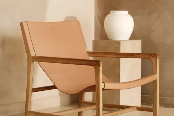 A designer leather armchair with warm beige limewash painted walls behind. There is a white vase on a pedestal at the rear.