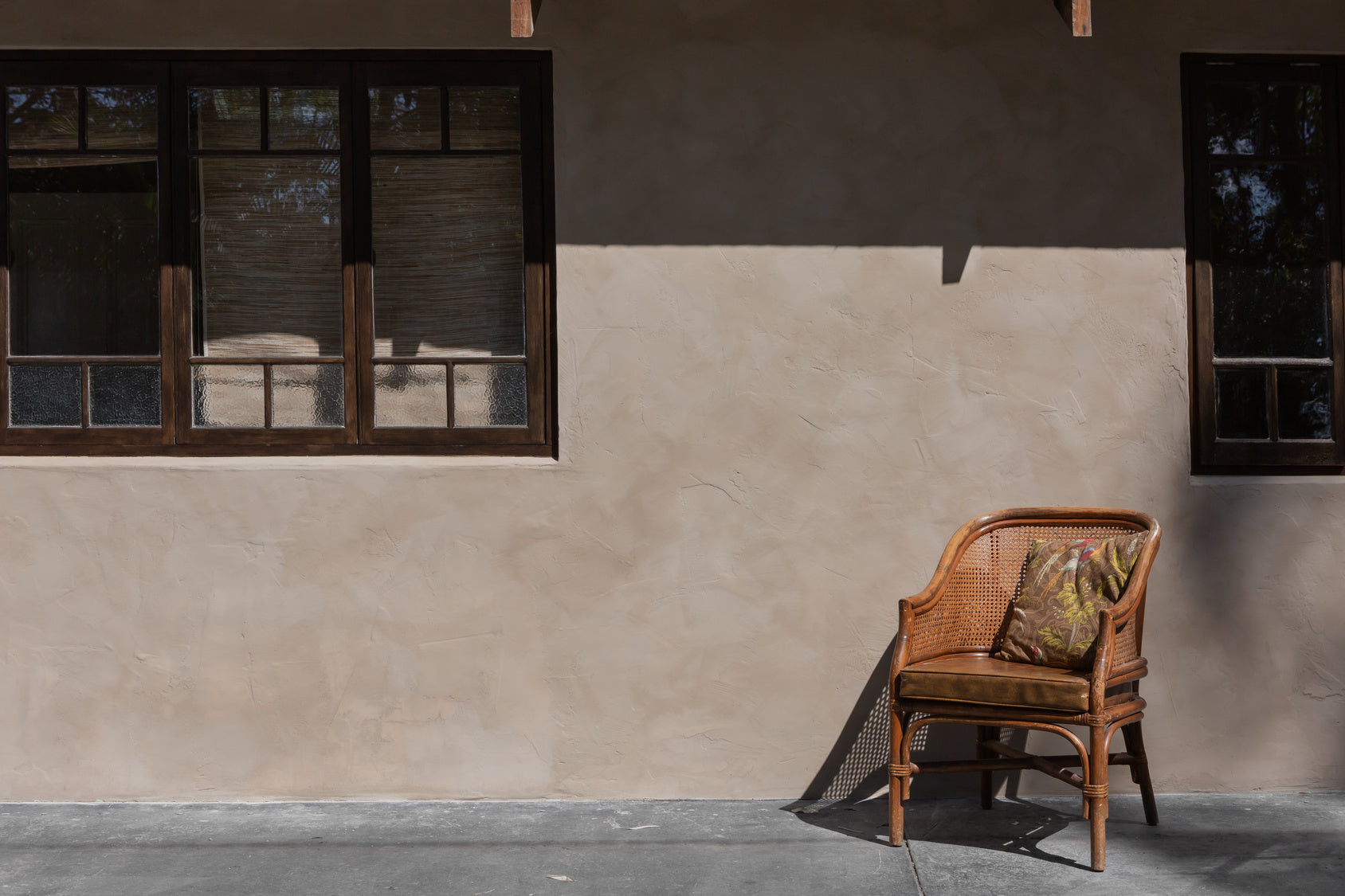 A rattan seat infront of brown limewash paint on an exterior wall
