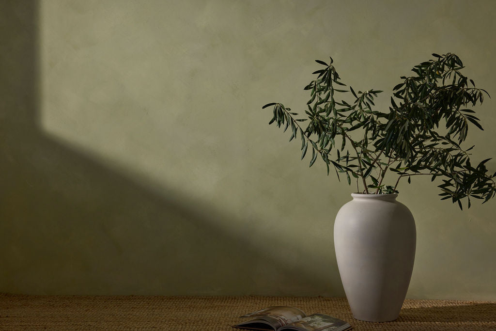 White vase with green plant on a textured surface against a plain wall