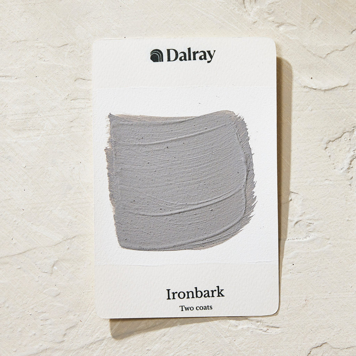 A Dalray paint swatch card labeled 'Ironbark' showing a textured gray paint stroke, placed on a light beige textured surface.