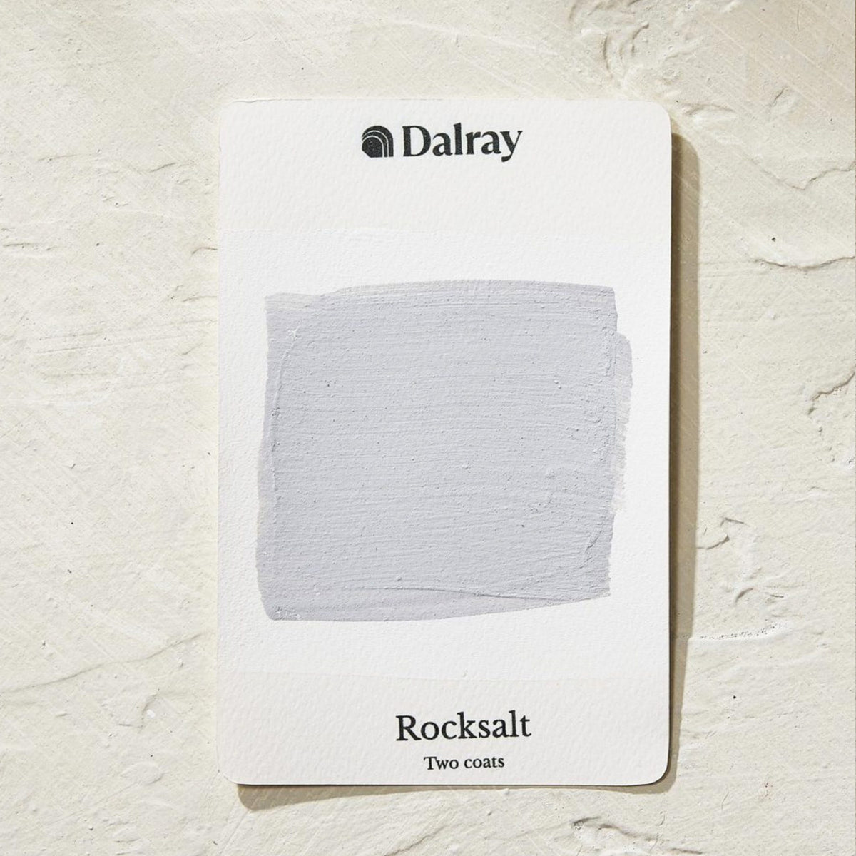 A Dalray limewash australia paint color card labeled 'Rocksalt' showing a light cool gray swatch on a white card, placed on a textured off-white surface.
