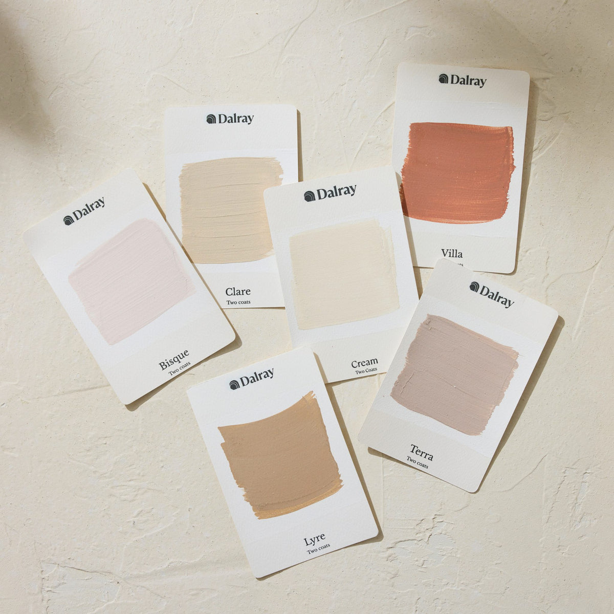 Six Dalray limewash paint swatch cards arranged on a textured cream surface, showing different neutral and warm beige shades including Rusque, Clare, Cream, Lyre, Villa, and Terra.