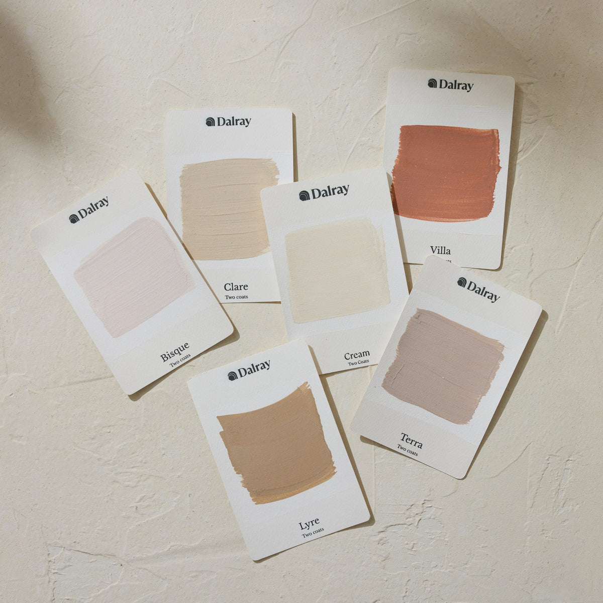 Six Dalray limewash paint swatch cards arranged on a textured off-white wall, showing different neutral and warm beige shades including Bisque, Clare, Villa, Cream, Lyre, and Terra.