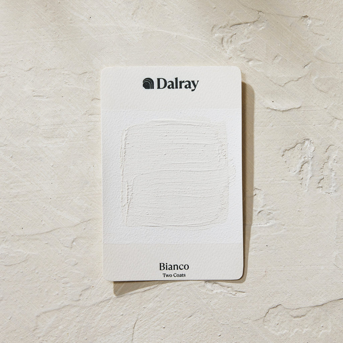 A Dalray Bianco Two Coat paint color card showing a textured white paint swatch, placed on a textured off-white plaster background.
