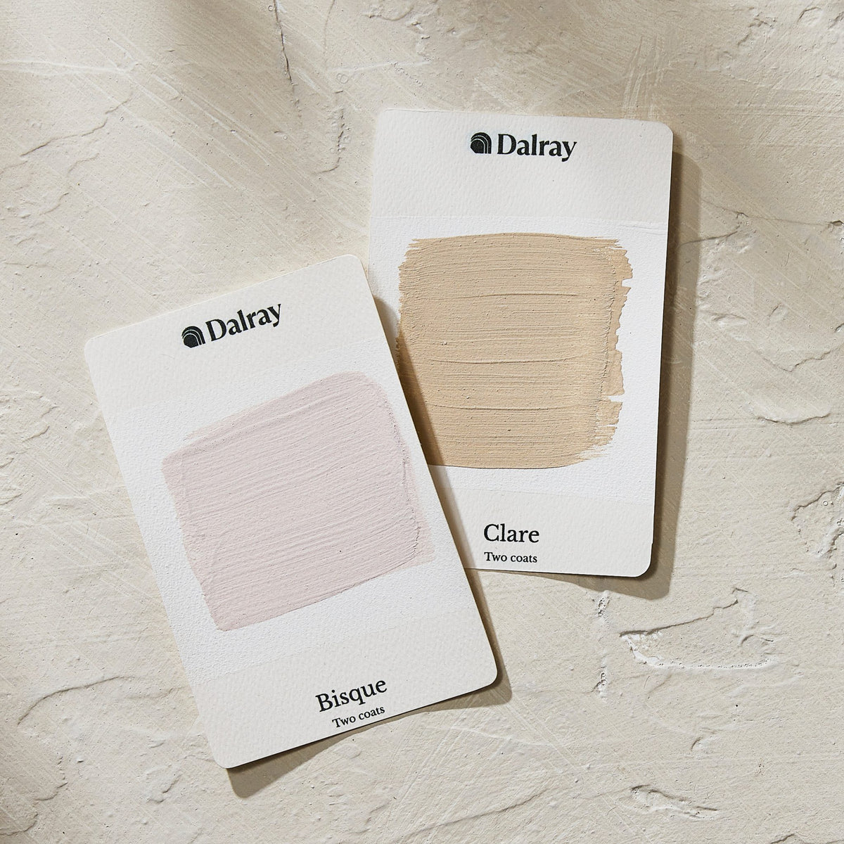 Two Dalray limewash swatch A6 cards on a textured off-white background, showing the shades Bisque (a pale pink-beige) and Clare (a light earthy beige).