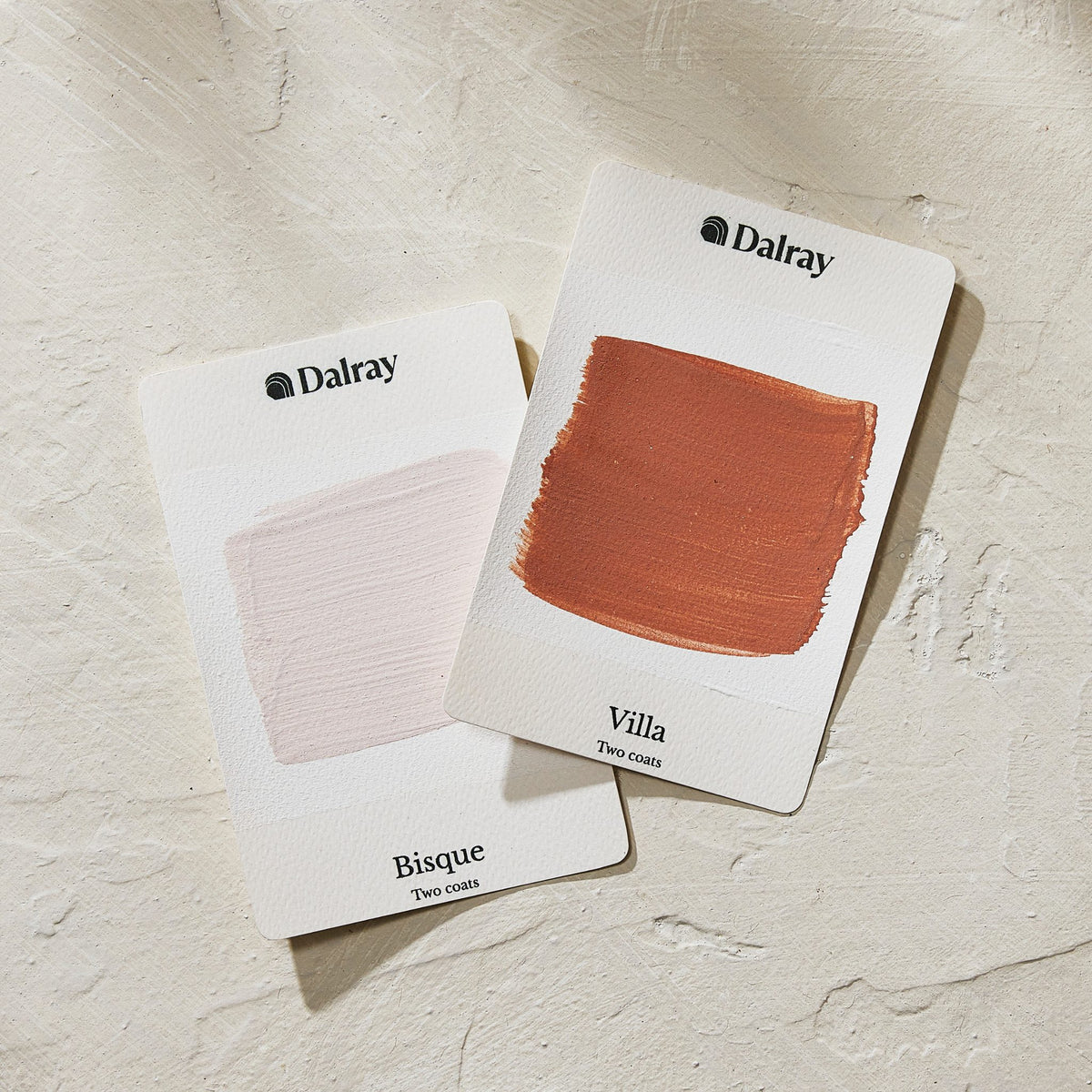 Two Dalray paint color cards on a textured off-white background. One card shows a pale pink swatch labeled Bisque, and the other shows a terracotta orange-brown swatch labeled Villa.