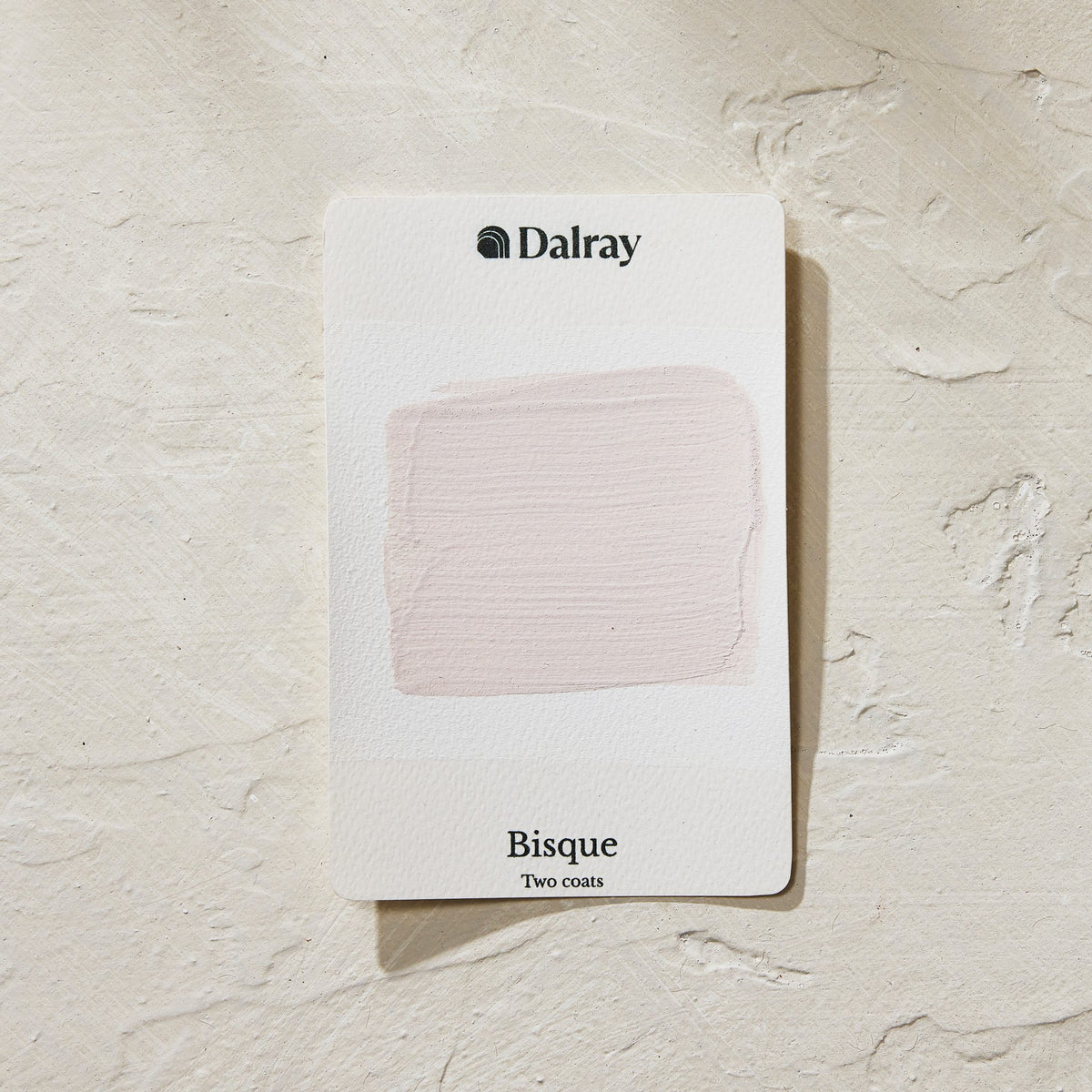A Dalray Bisque two-coat paint swatch card showing a light pink textured paint stroke, set against a textured off-white background.