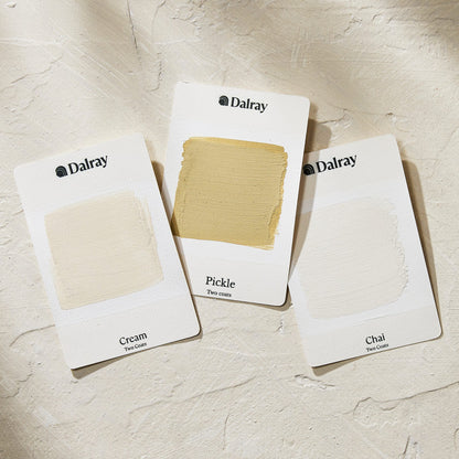 Three Dalray paint swatch cards labeled Cream, Pickle, and Chai, arranged on a textured off-white surface. The center card shows a warm beige paint swatch, while the other two show neutral beige paint swatches.