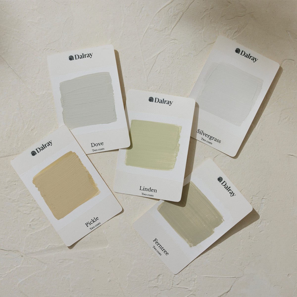 Five Dalray color sample cards of limewash paint greens with painted color blocks and labeled shades (Dove, Silvergrass, Peale, Linden, Ferree) arranged on a textured off-white surface.
