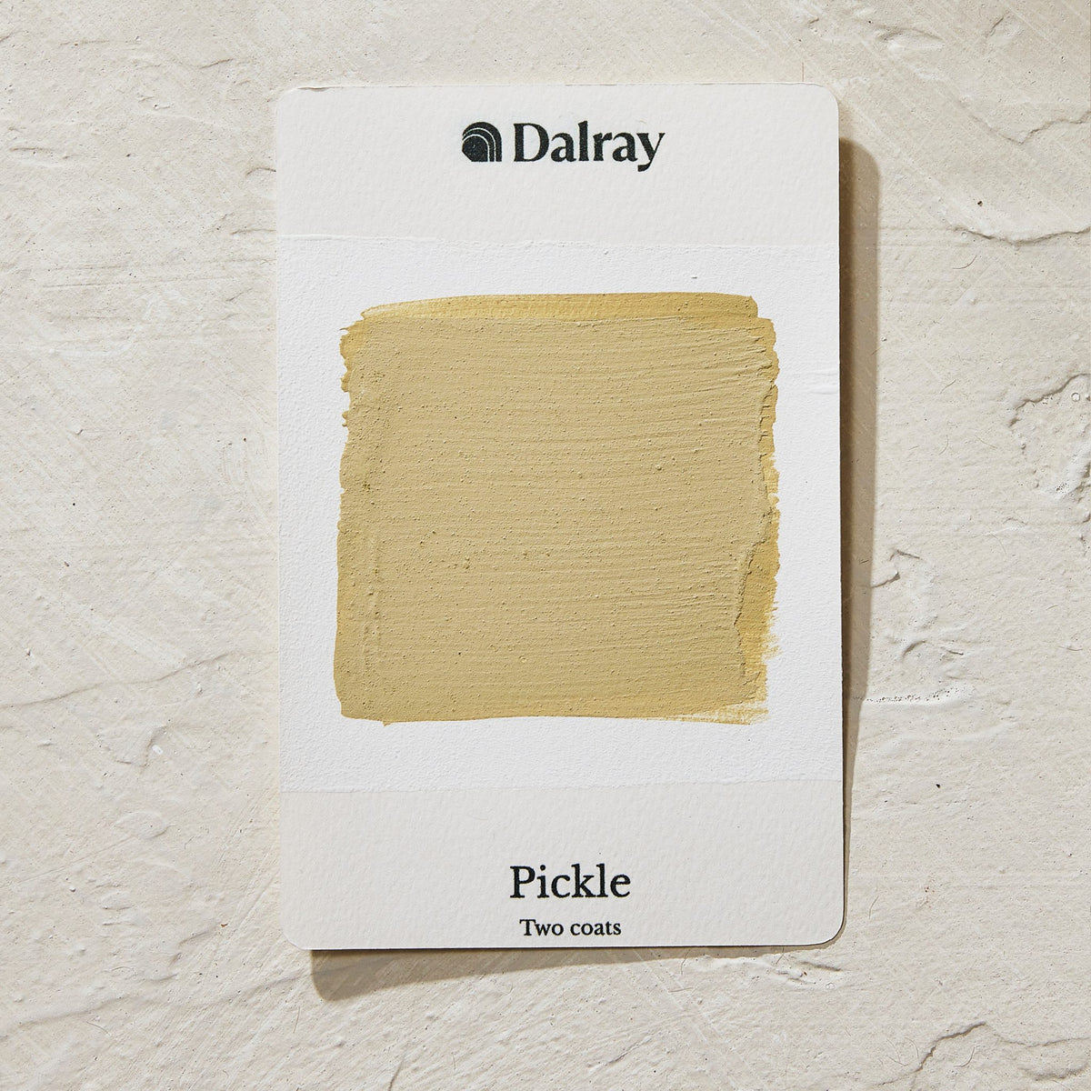 A Dalray paint swatch card labeled 'Pickle Two coats' showing a textured beige-yellow mustard paint swatch on a white card, set against a textured off-white background.