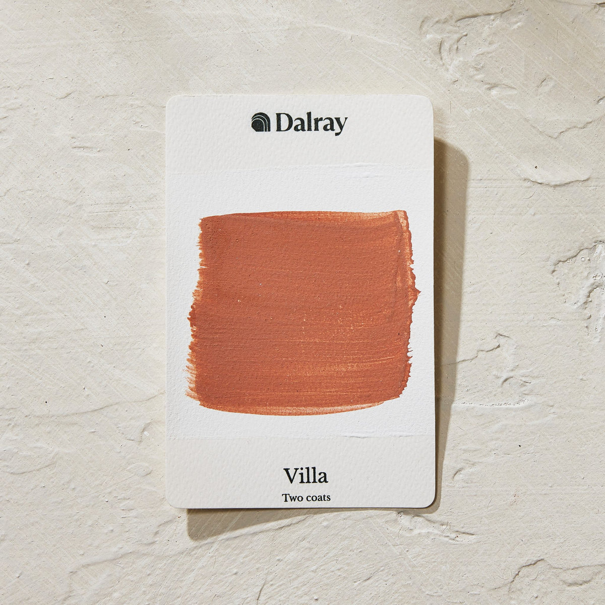 A Dalray paint swatch card labeled 'Villa Two coats' showing a warm terracotta orange-brown paint swatch on a white card, placed on a textured off-white surface.