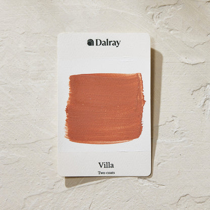 A Dalray paint swatch card labeled 'Villa Two coats' showing a warm terracotta orange-brown paint swatch on a white card, placed on a textured off-white surface.