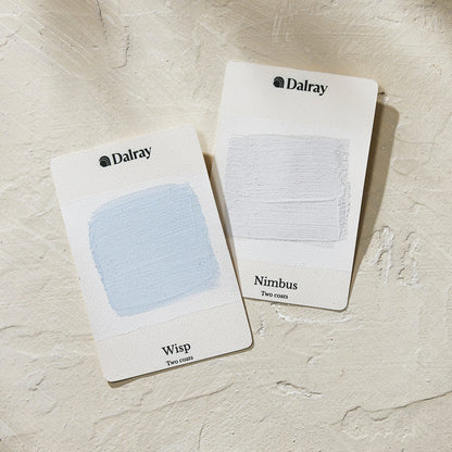 Two Dalray paint swatch cards, labeled Wisp (a pale blue swatch) and Nimbus (a very light cool gray swatch), displayed on a textured beige surface.