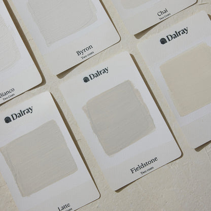 A close-up of several Dalray limewash paint swatch cards arranged on a light textured surface. The visible cards show painted color samples and printed names including Byron, Chai, Fieldstone, and Latte.