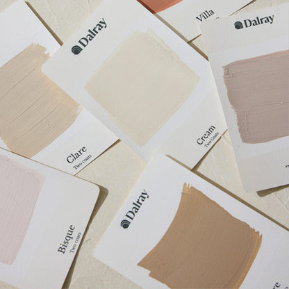 A flat-lay arrangement of Dalray cream and warm and neutral limewash swatch cards, showing various shades including Clare, Cream, Villa, and Bisque on a textured beige background.