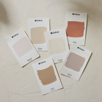 Six Dalray limewash paint swatch cards arranged on a textured off-white wall, showing different neutral and warm beige shades including Bisque, Clare, Villa, Cream, Lyre, and Terra.