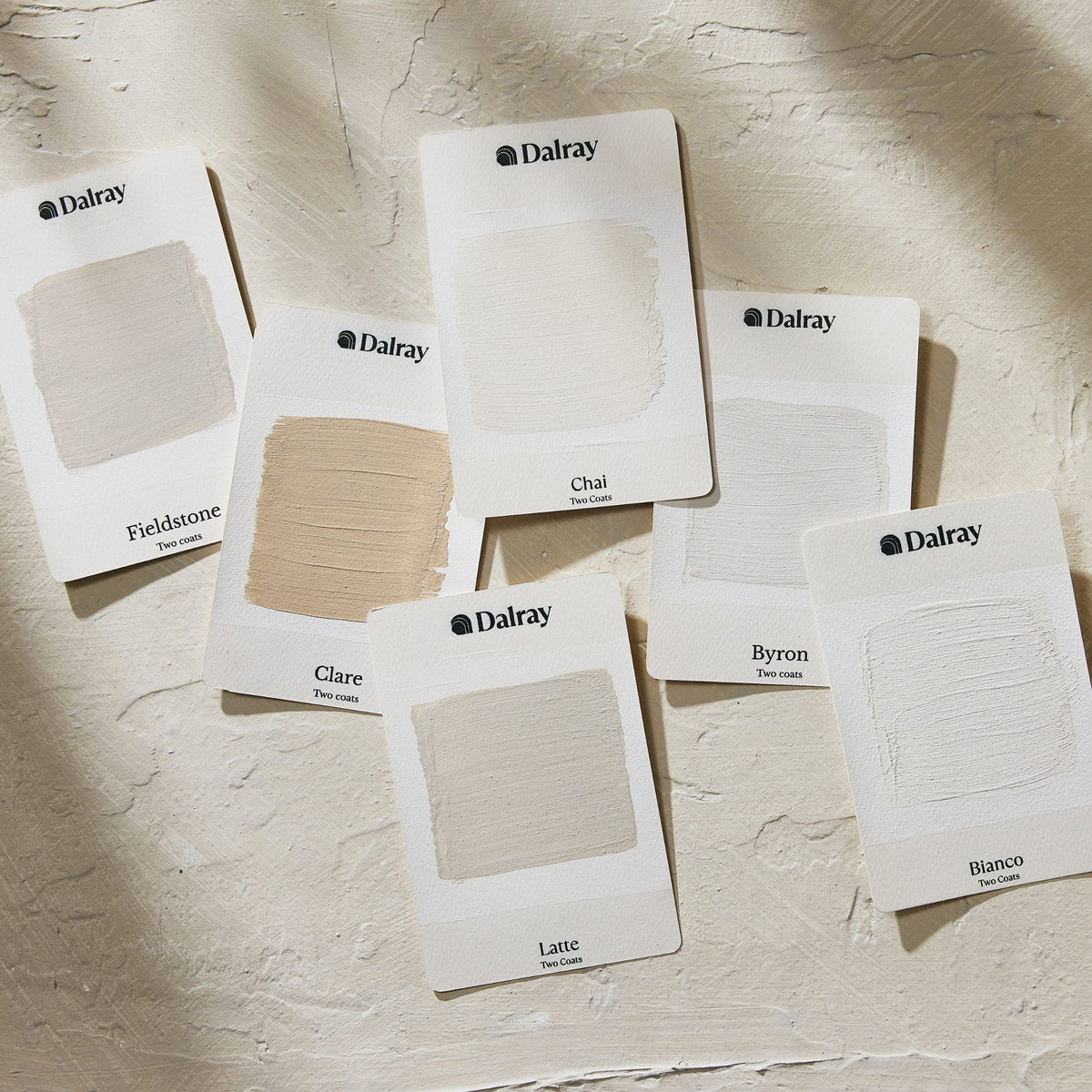 Six Dalray neutral limewash paint swatch cards arranged on a textured off-white surface, showing different neutral shades including Fieldstone, Chai, Clare, Byron, and Bianco.