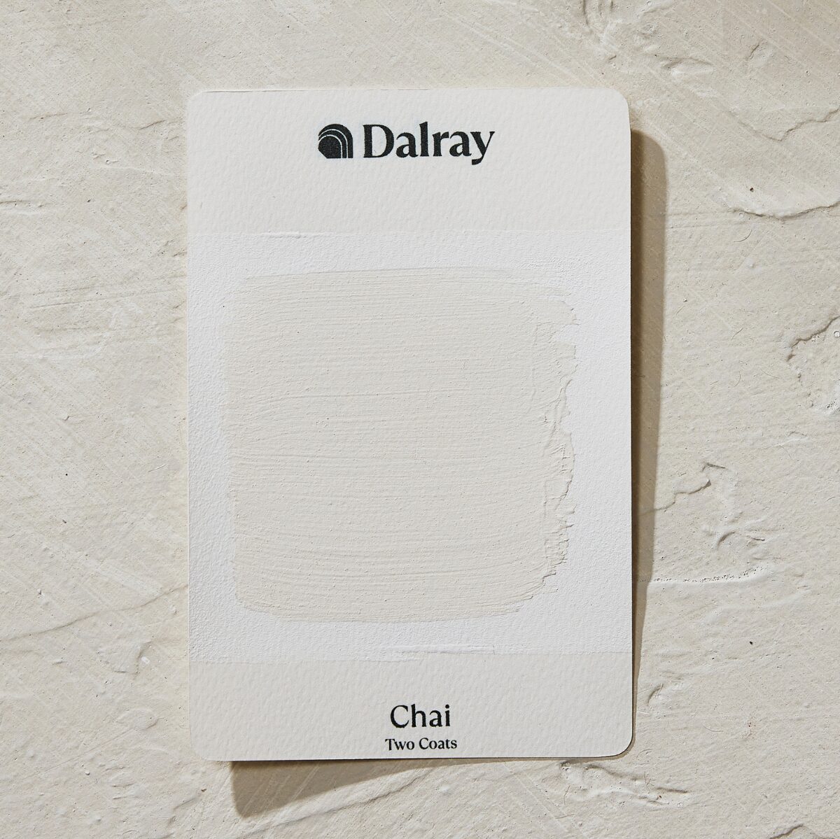 A Dalray paint swatch card labeled 'Chai Two Coats' showing a textured off-white limewash paint swatch, placed on a matching textured off-white surface.