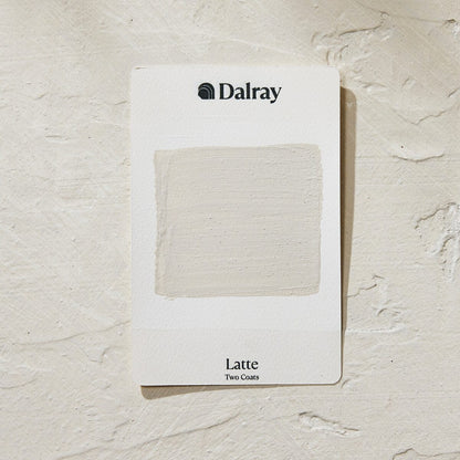 A Dalray warm paint swatch card labeled 'Latte Two Coats' showing a textured off-white neutral paint sample, placed on a textured off-white surface.