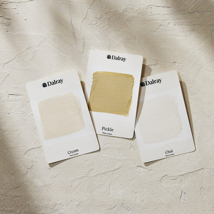 Three Dalray warm limewash paint swatch cards labeled Cream, Pickle, and Chal, arranged on a textured off-white surface with soft shadows.