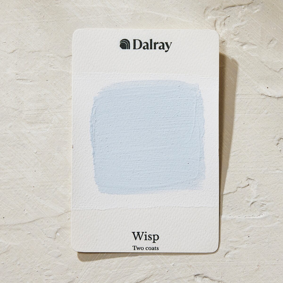 A Dalray paint swatch card labeled 'Wisp Two coats' showing a light icy blue limewash painted swatch on a white card, placed on a textured off-white surface.