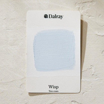 A Dalray paint swatch card labeled 'Wisp Two coats' showing a light icy blue limewash painted swatch on a white card, placed on a textured off-white surface.